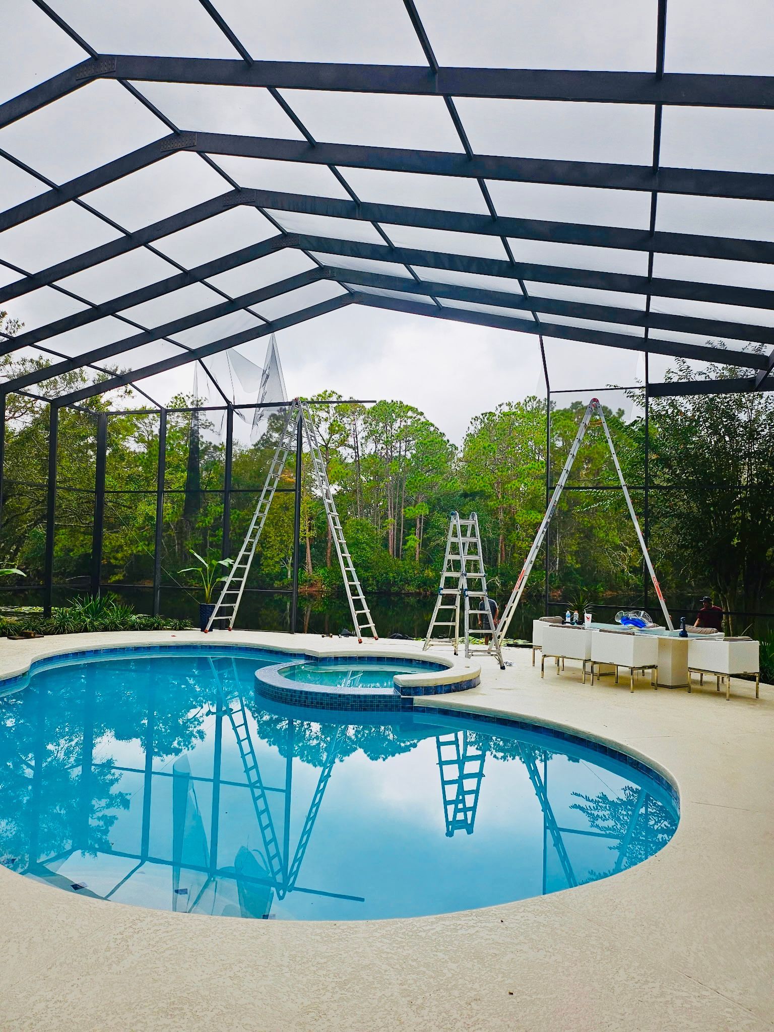 Screened backyard pool with ladders, white chairs, and trees