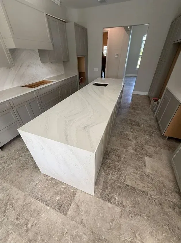 Modern kitchen with long white island and gray cabinets. Light gray tiled floor.