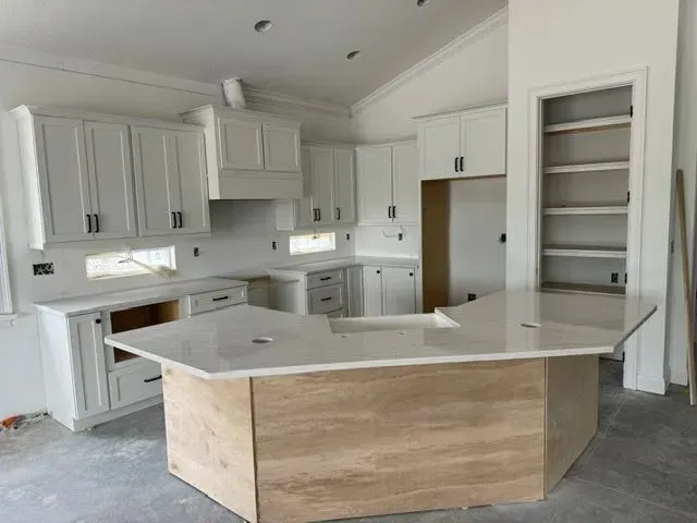 Unfinished white kitchen with cabinets, island, and countertops. Construction in progress.