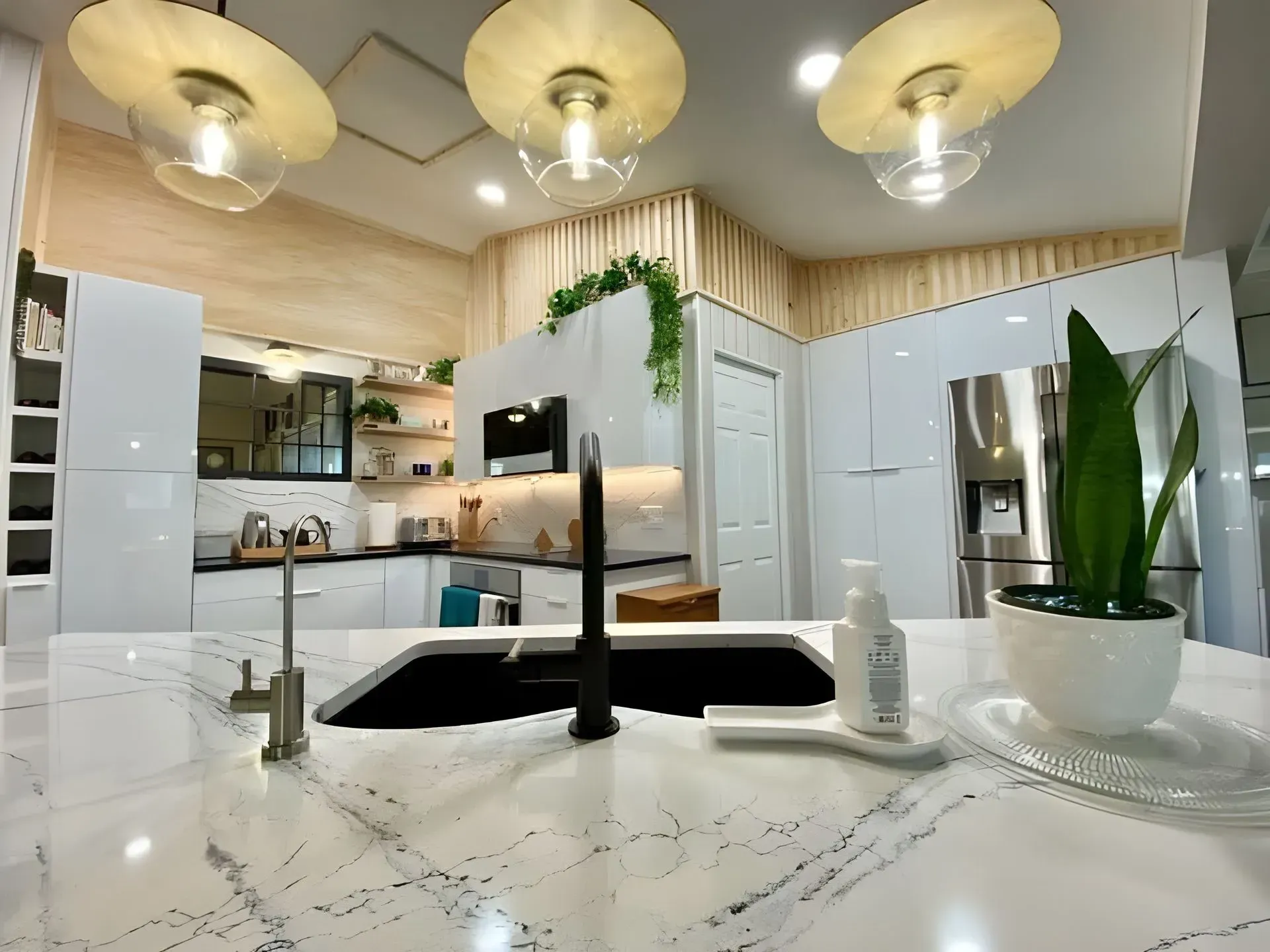 Modern white kitchen with island, marble countertops, pendant lights, and stainless steel appliances.