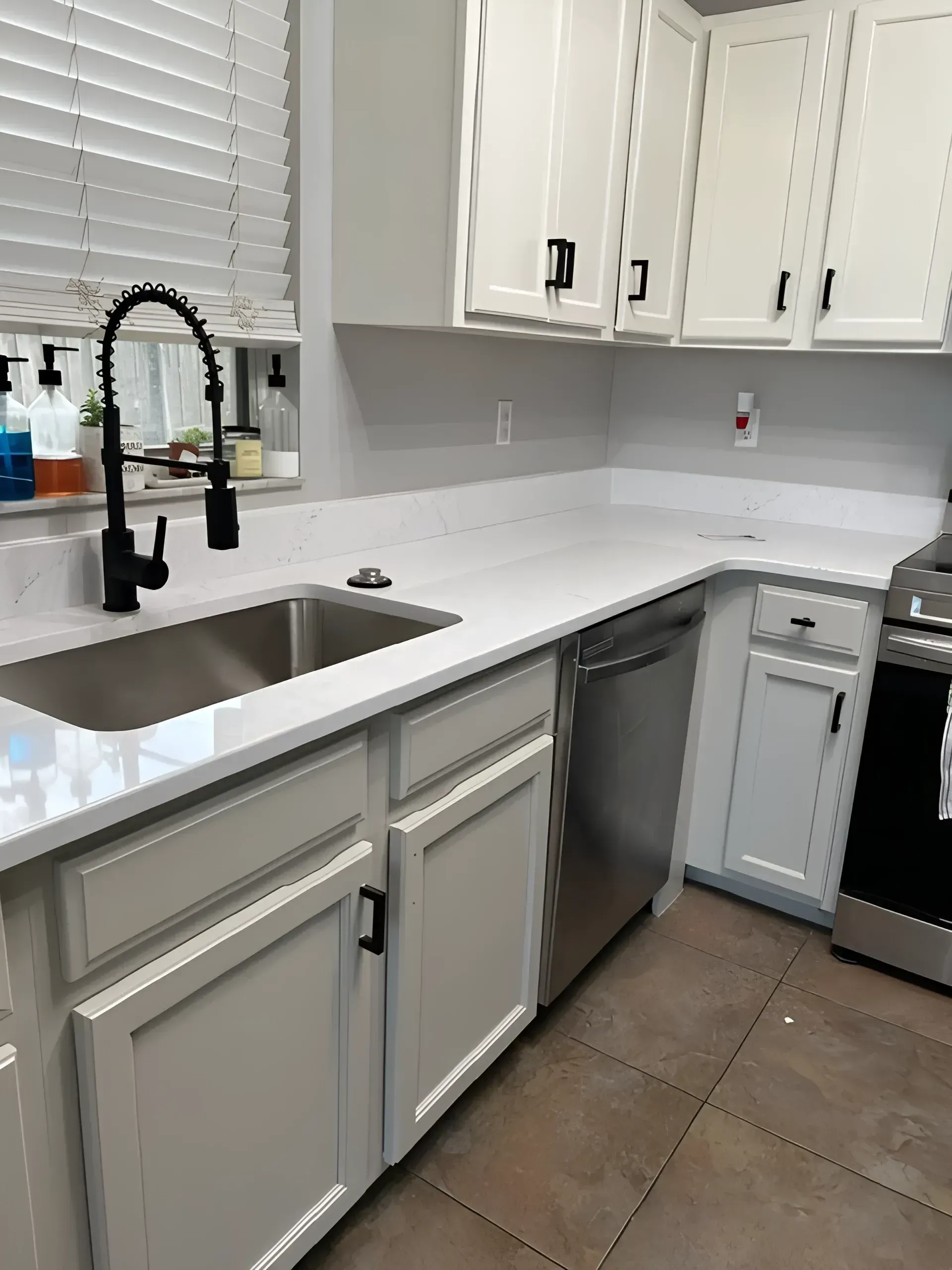 White kitchen with countertop, cabinets, and appliances. Black faucet. Light gray backsplash.