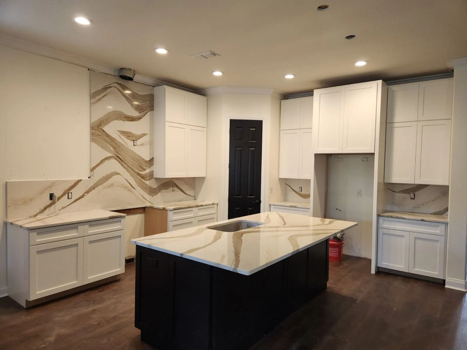 Kitchen with white cabinets, dark island, beige and brown patterned backsplash and countertops.