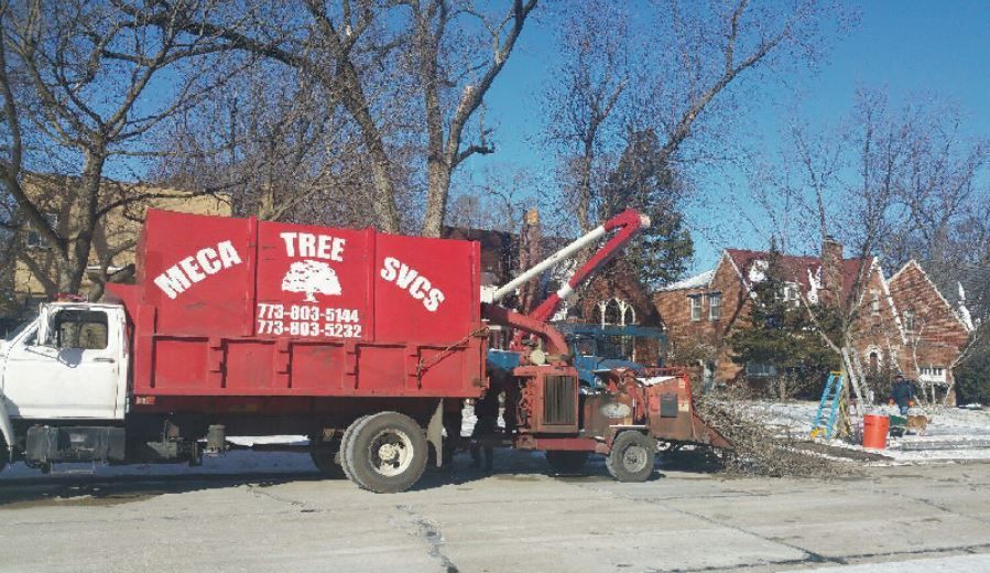 A red Meca Tree Svcs truck with an attached wood chipper parked on a residential street in winter.