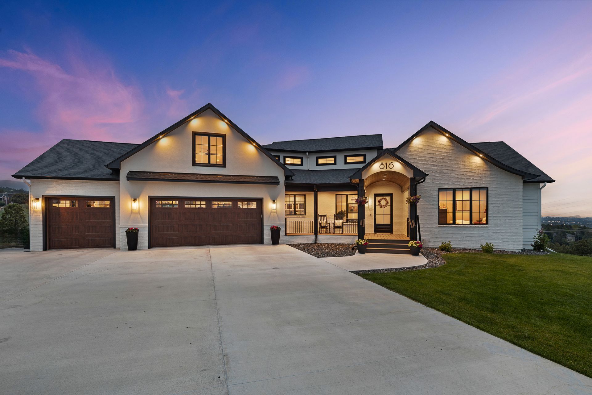 Modern white house with brown garage doors, porch, and a concrete driveway under a purple and pink sunset.