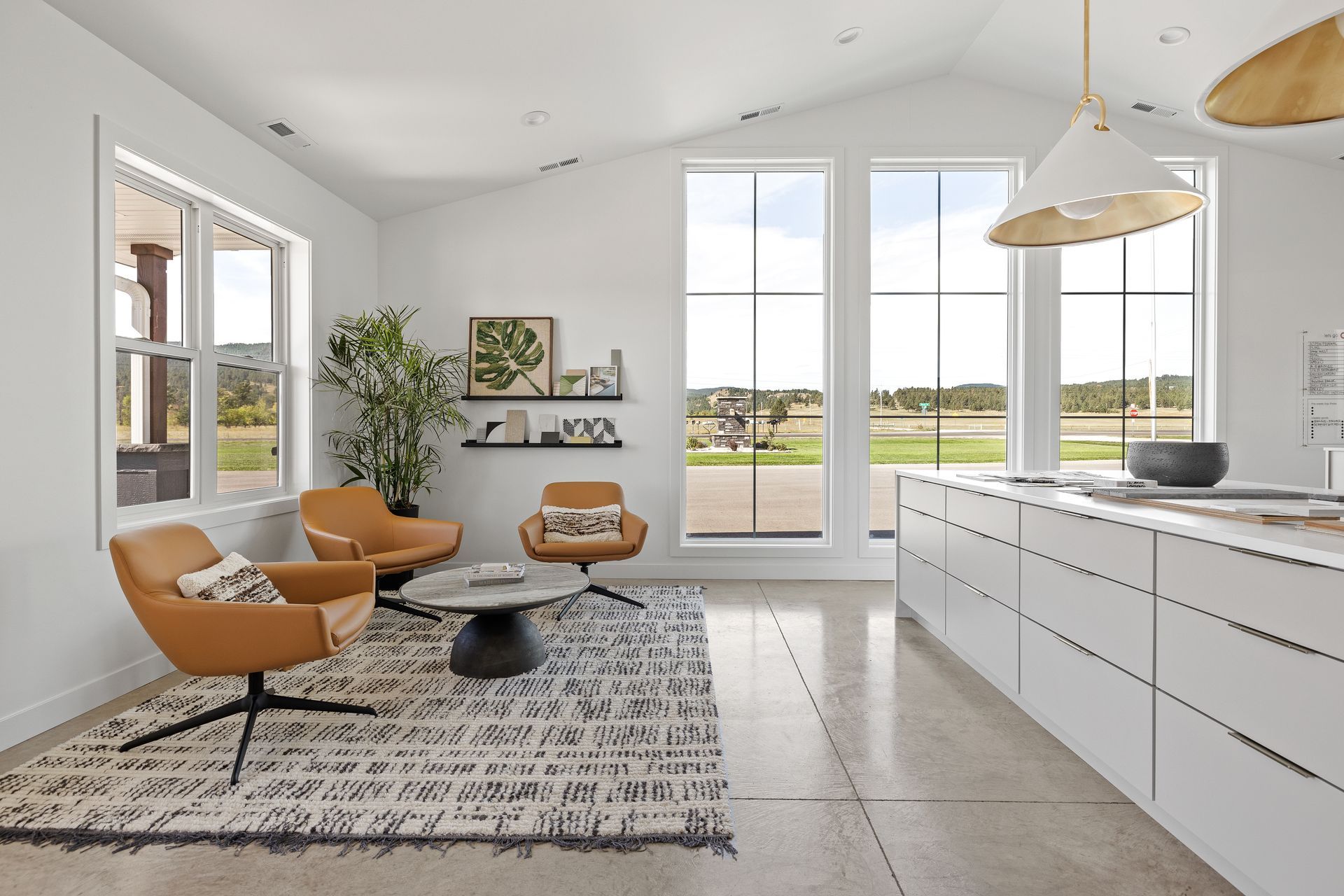 Modern living room with tan swivel chairs, area rug, tall windows, and white kitchen island.