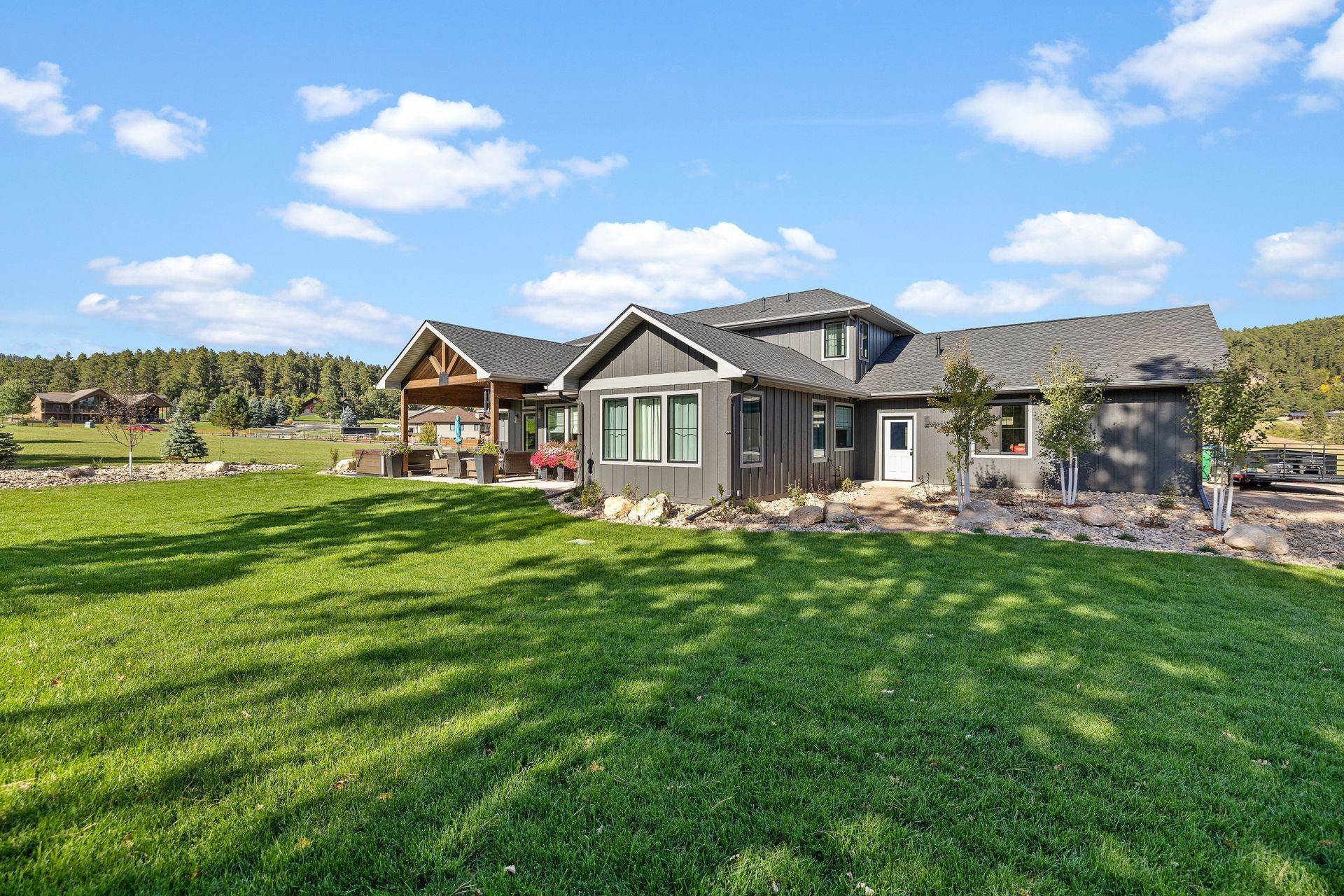 Gray house with green lawn, blue sky, and trees.