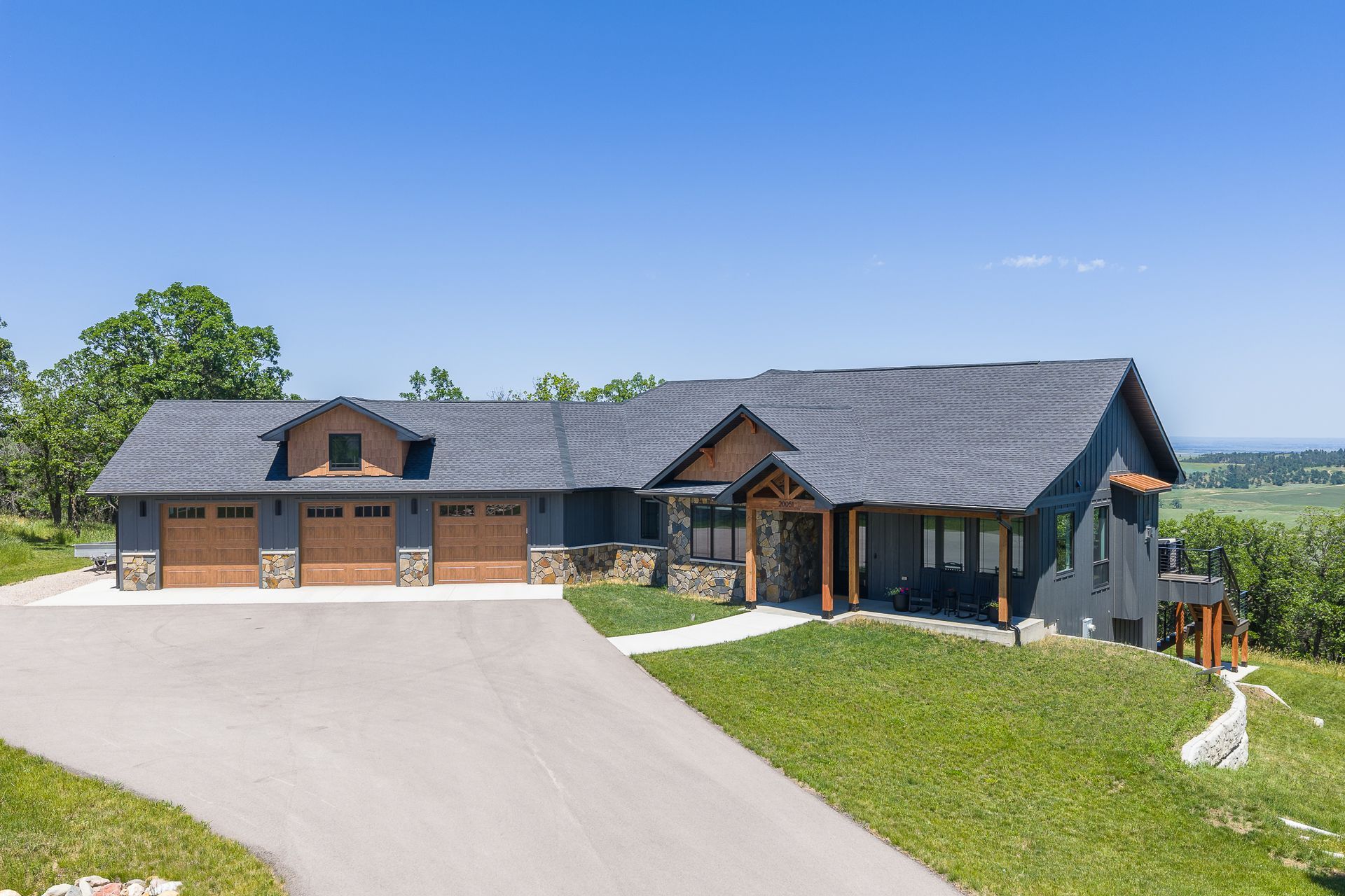 Modern gray house with brown garage doors and a long driveway on a grassy hill.