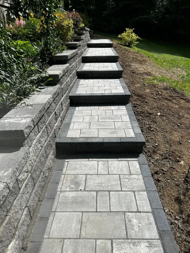 Stone steps and pathway ascending a hillside, bordered by a retaining wall and grass.