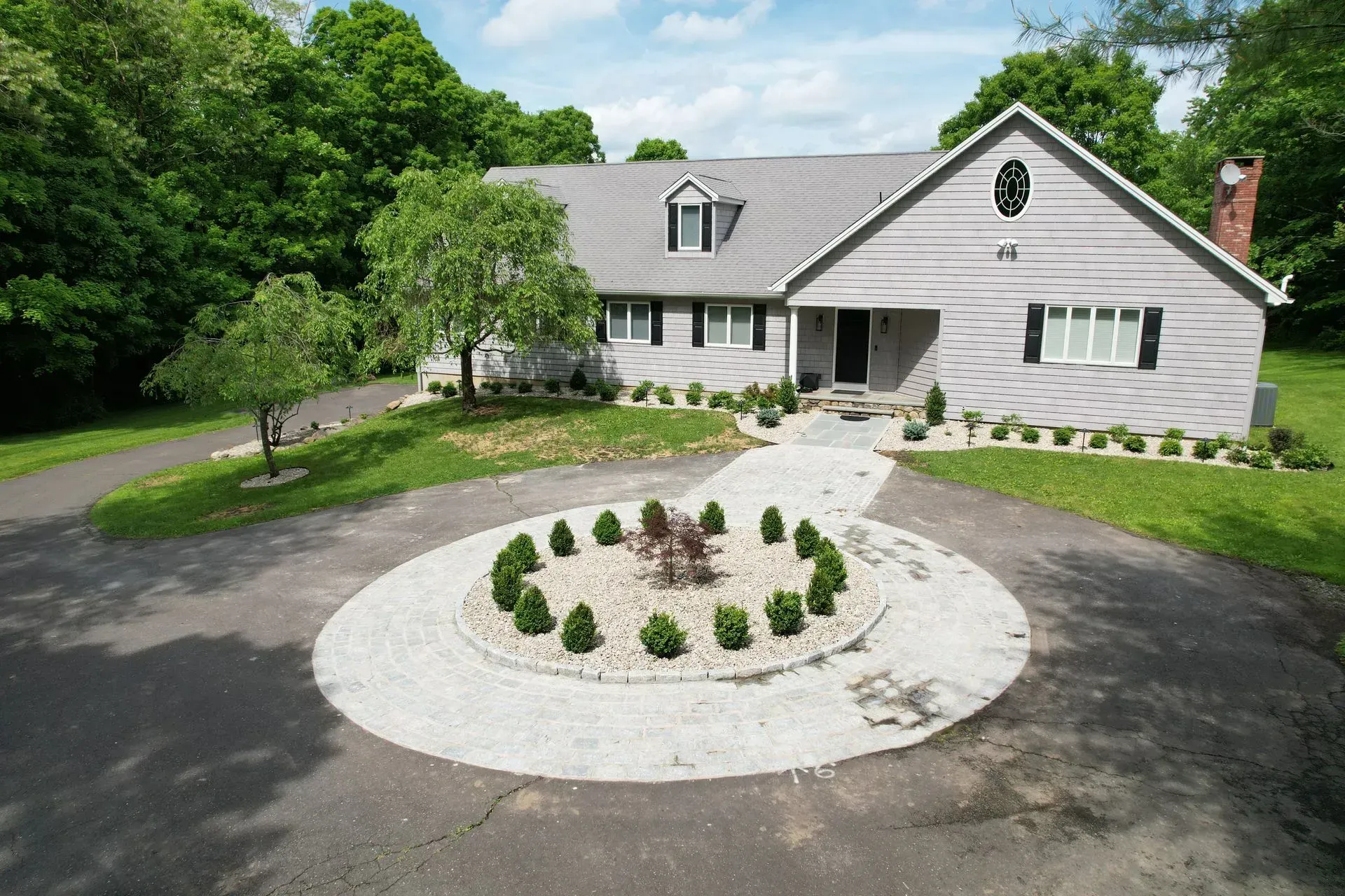 House with gray siding and circular driveway with landscaping.