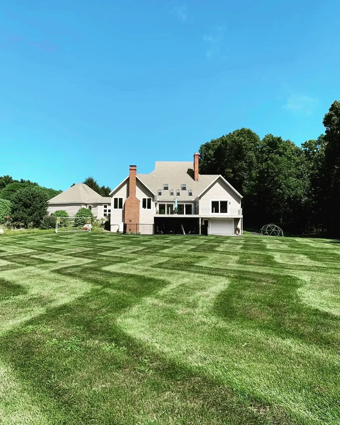 House with zigzag lawn mowing pattern under a bright blue sky.