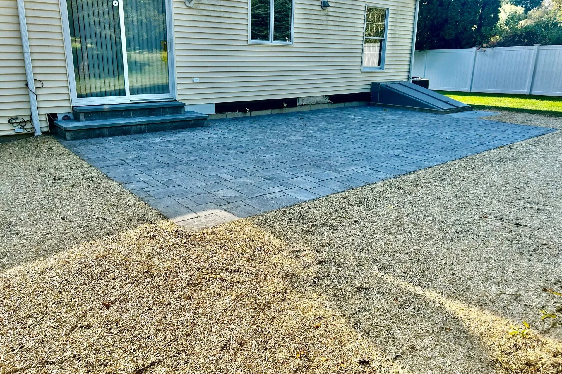 A gravel patio with a dark brick area near a house with a sliding glass door and ramp.