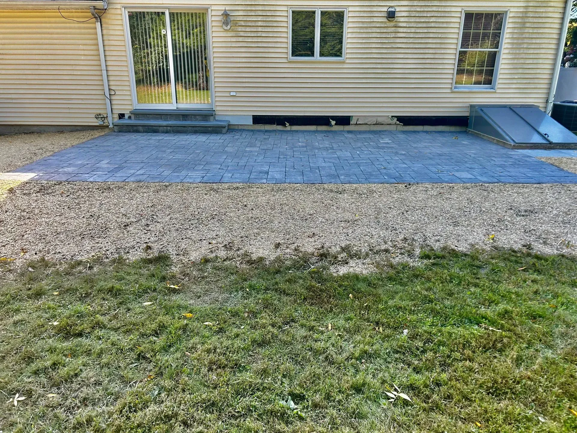 Backyard patio with grey pavers, gravel border, and a building with a sliding door.
