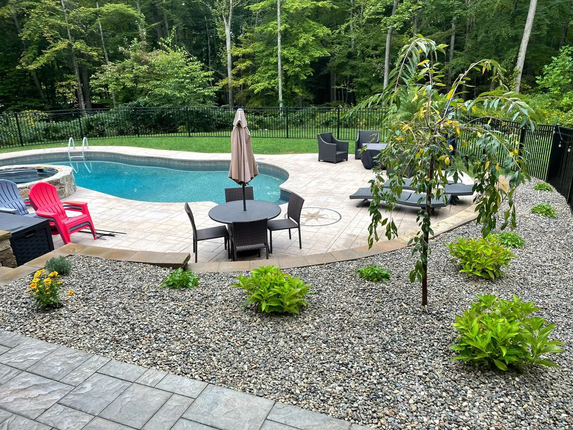 Backyard with pool, patio, and stone landscaping. Furniture includes dining table, chairs, and lounge chairs.