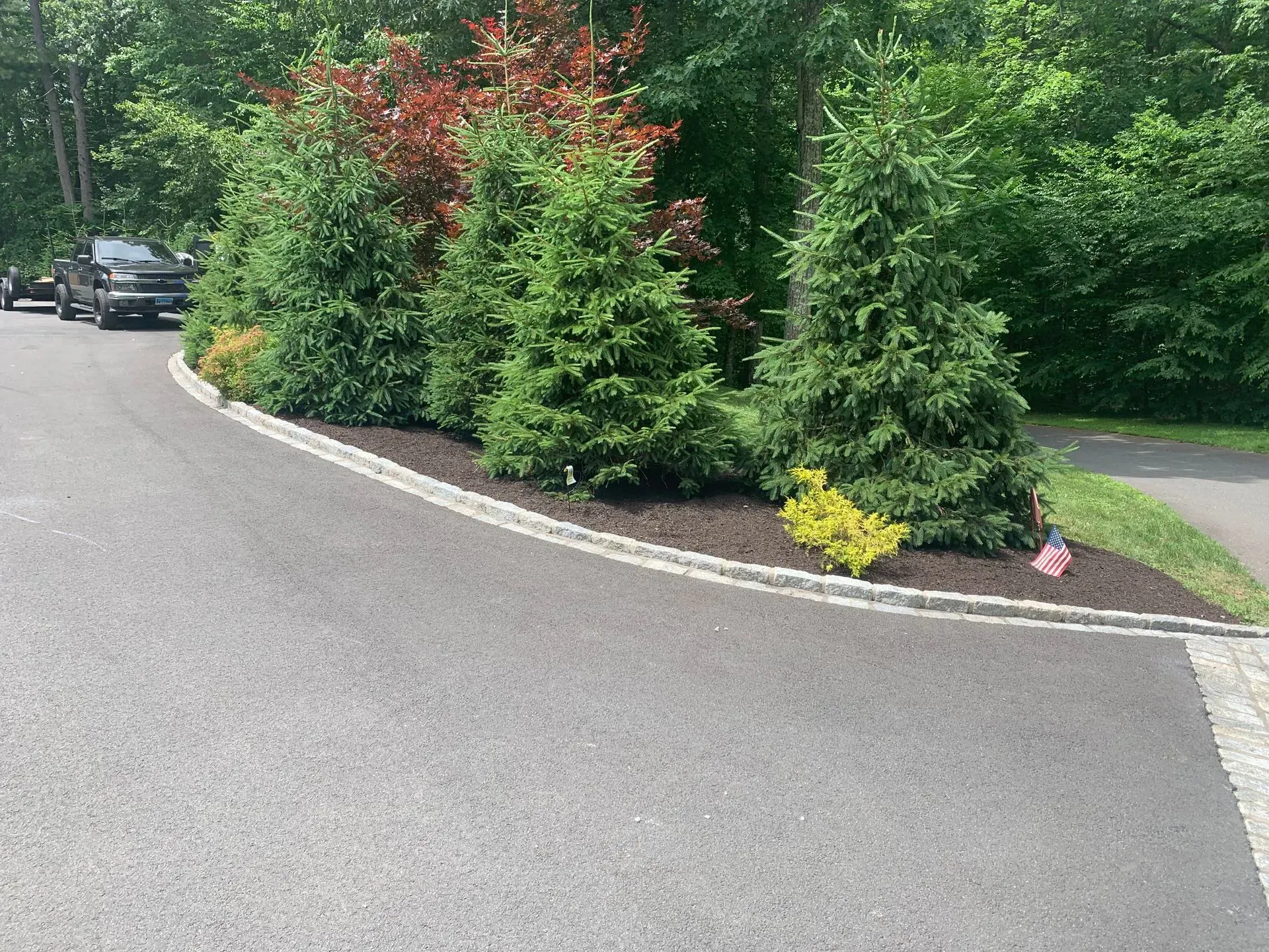 Driveway with green and red trees in a landscaped bed, bordered by a stone edge.