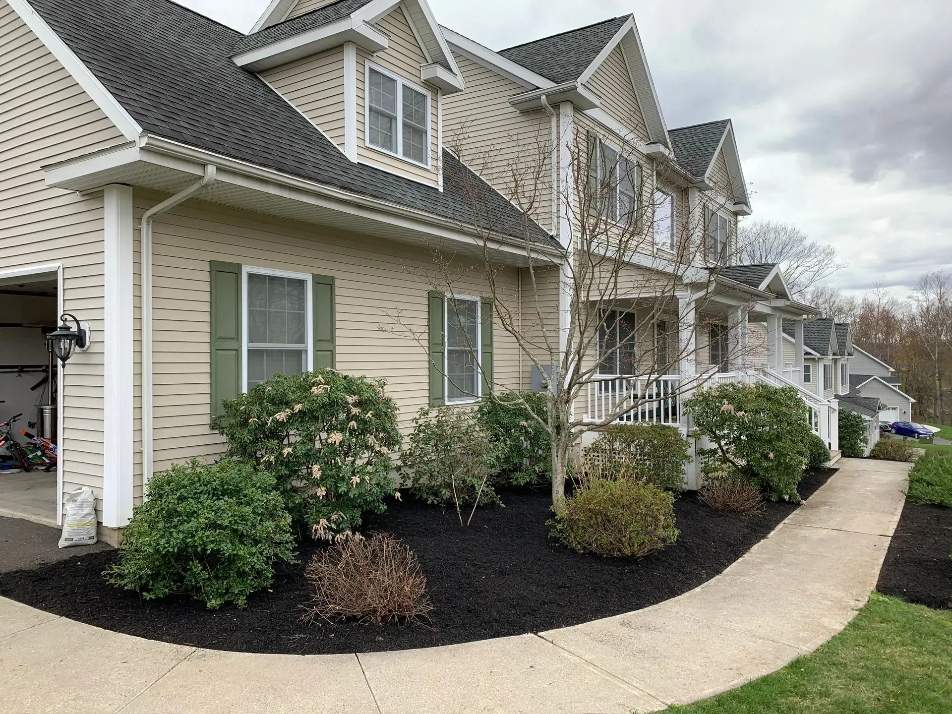 Beige house with green shutters, black mulch, and a concrete walkway.