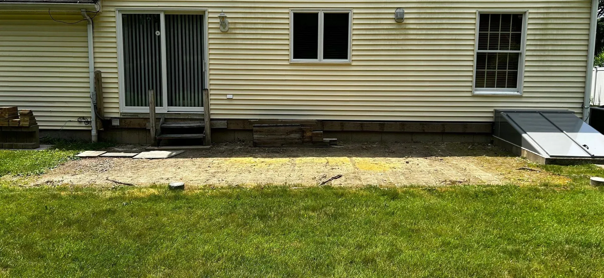 Back of a beige house with a sliding glass door, two windows, and a basement door. Grass and gravel in foreground.