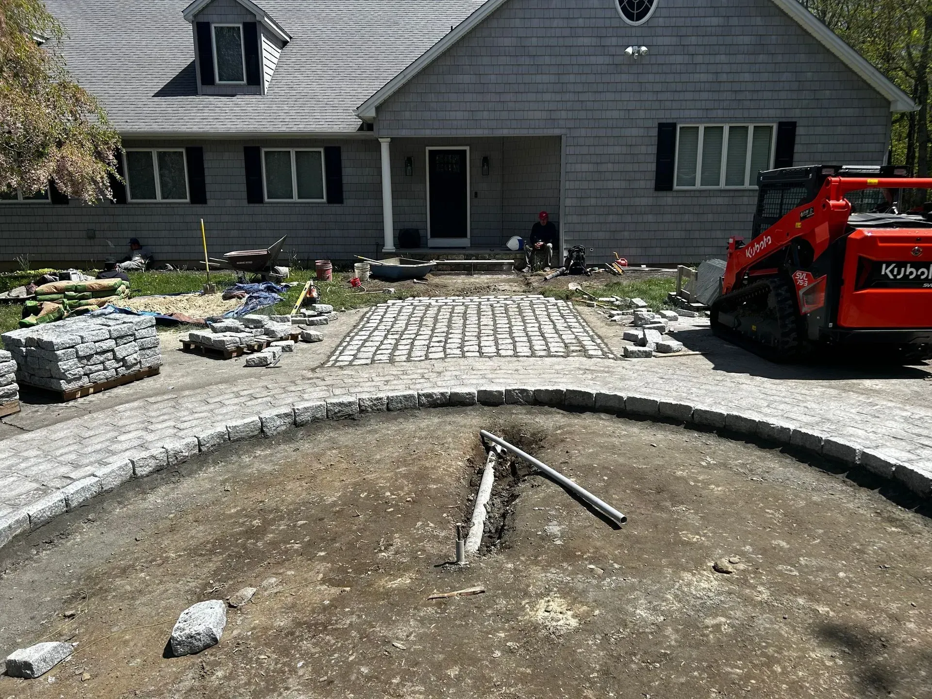 Construction site: A house with a driveway under construction. A small red excavator is present.