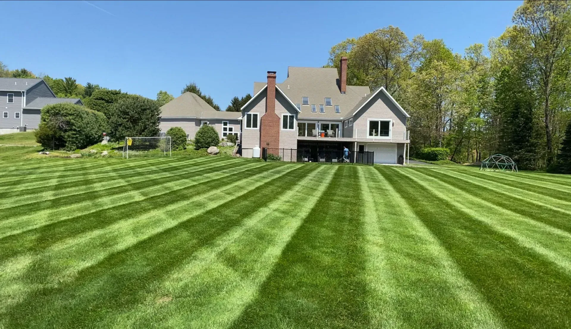 Green striped lawn in front of a large house under a clear, blue sky.