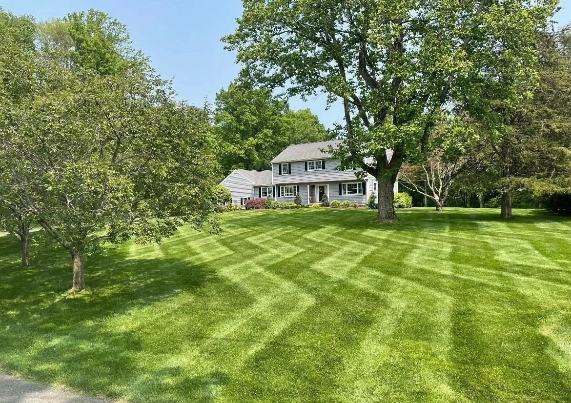 A house sits in the background of a lush, green lawn featuring an intricate zigzag pattern mown into the grass.