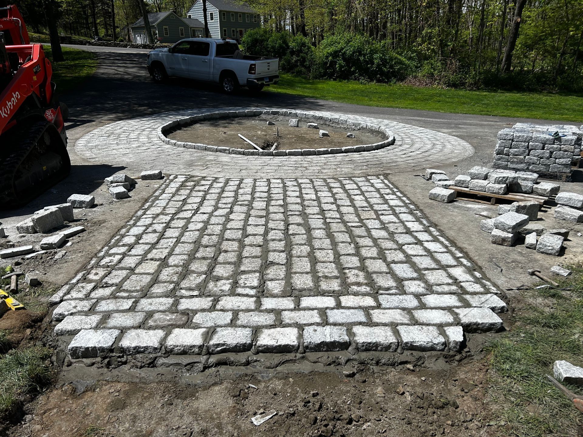 A stone paver driveway under construction featuring a rectangular walkway section leading to a circular center.