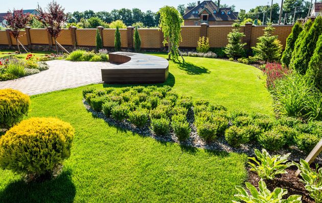 A well-manicured garden with a stone pathway, green lawn, and various shrubs and trees.