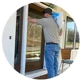 Man carries package to a home's front door; he wears a cap, jeans, and a t-shirt.