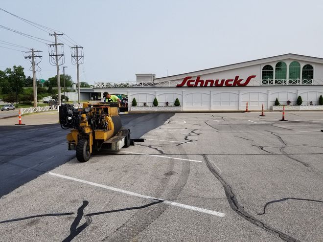 Yellow road-marking machine repaints parking lines in a store lot with a Schnucks storefront behind it