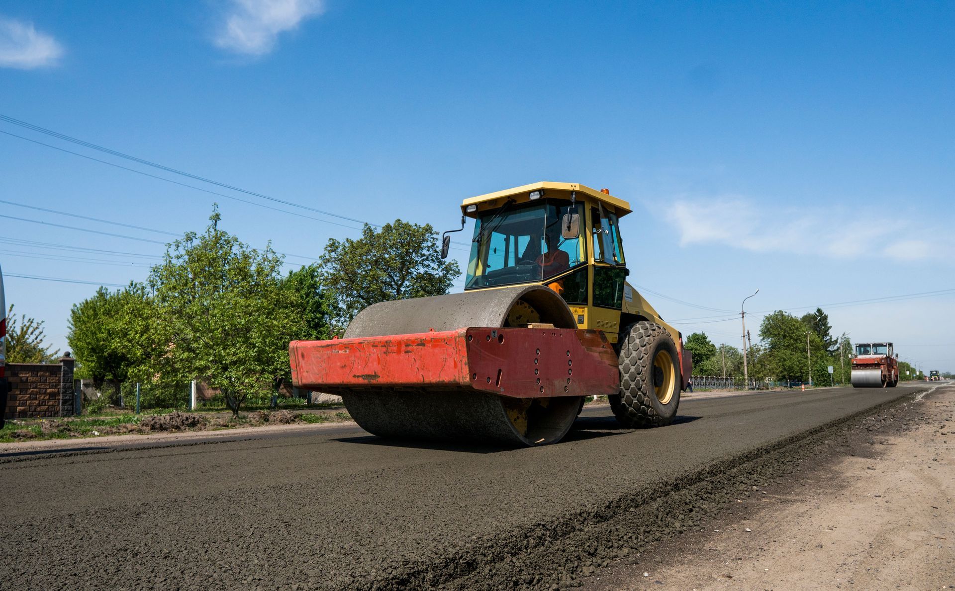 Yellow road roller paving a dark asphalt road under a blue sky