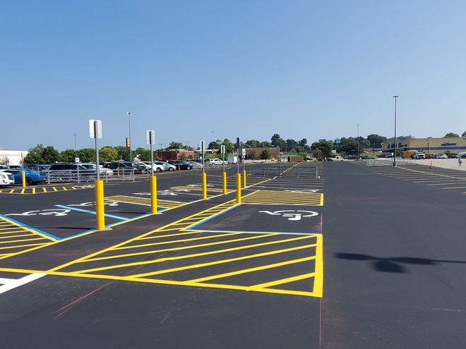 Empty parking lot with yellow-striped accessible spaces and blue handicap signs under a clear sky