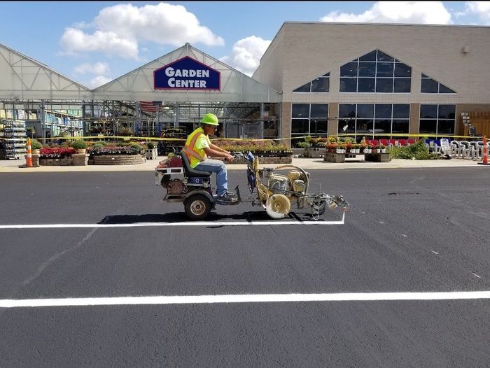 A worker on a riding mower is painting a white line in front of a shopping center.