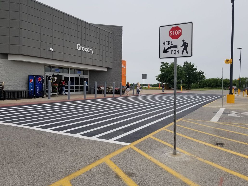 Store entrance with zebra-striped pedestrian crossing and stop sign in a parking lot.
