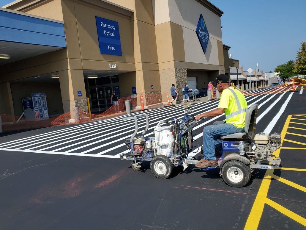 Worker painting yellow stripes on a crosswalk outside a store entrance
