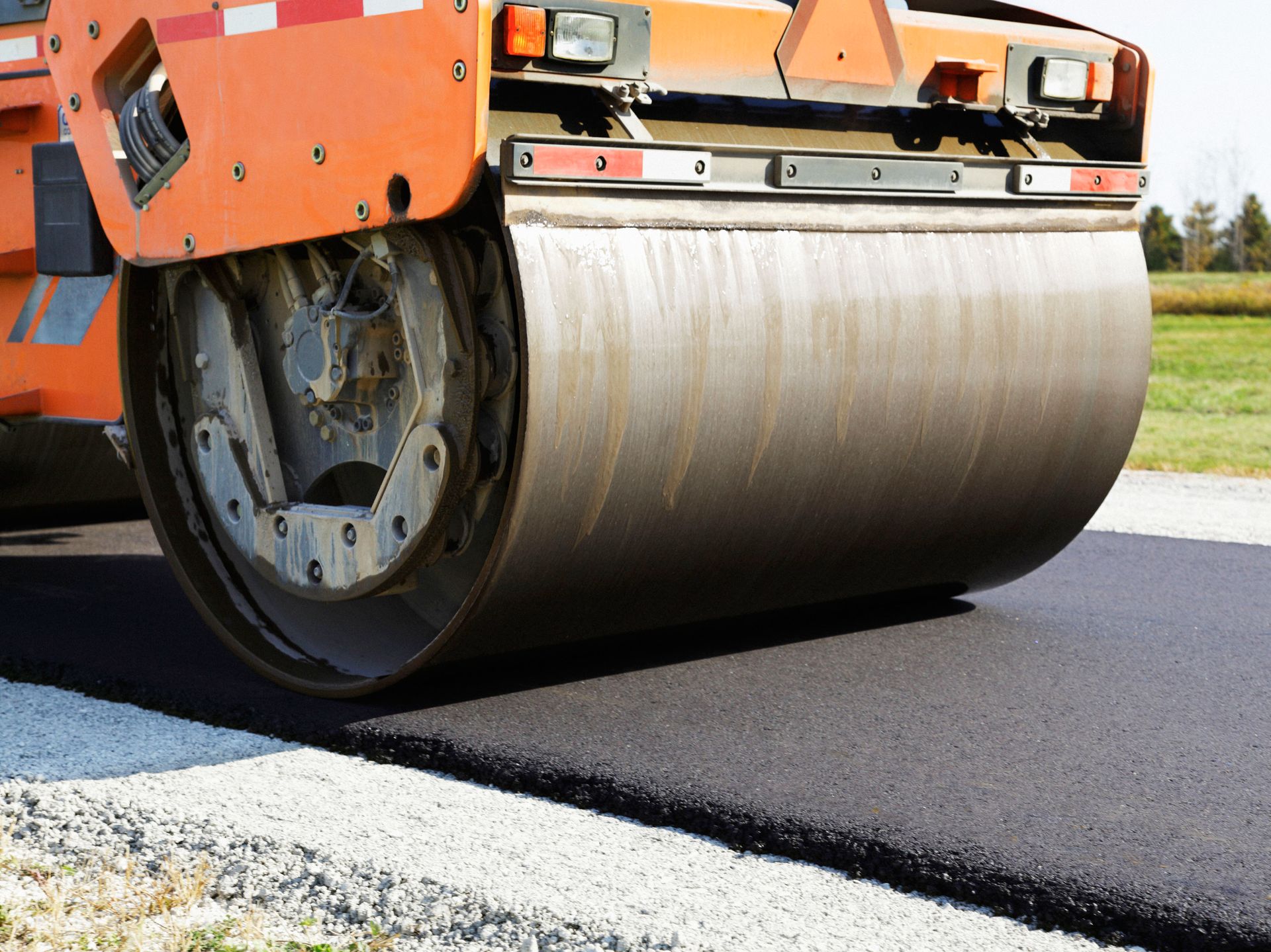 Orange road roller compacting fresh asphalt on a street