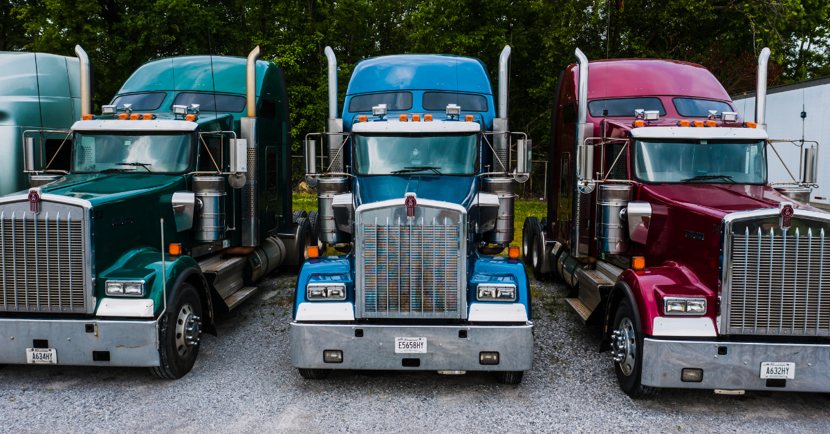 Three colorful semi-trucks parked side-by-side: green, blue, and burgundy.