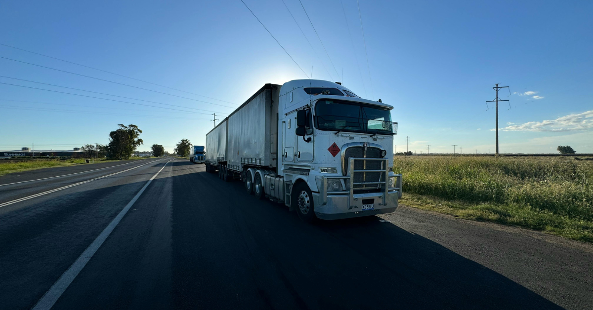 White semi-truck on highway with sun in the background.