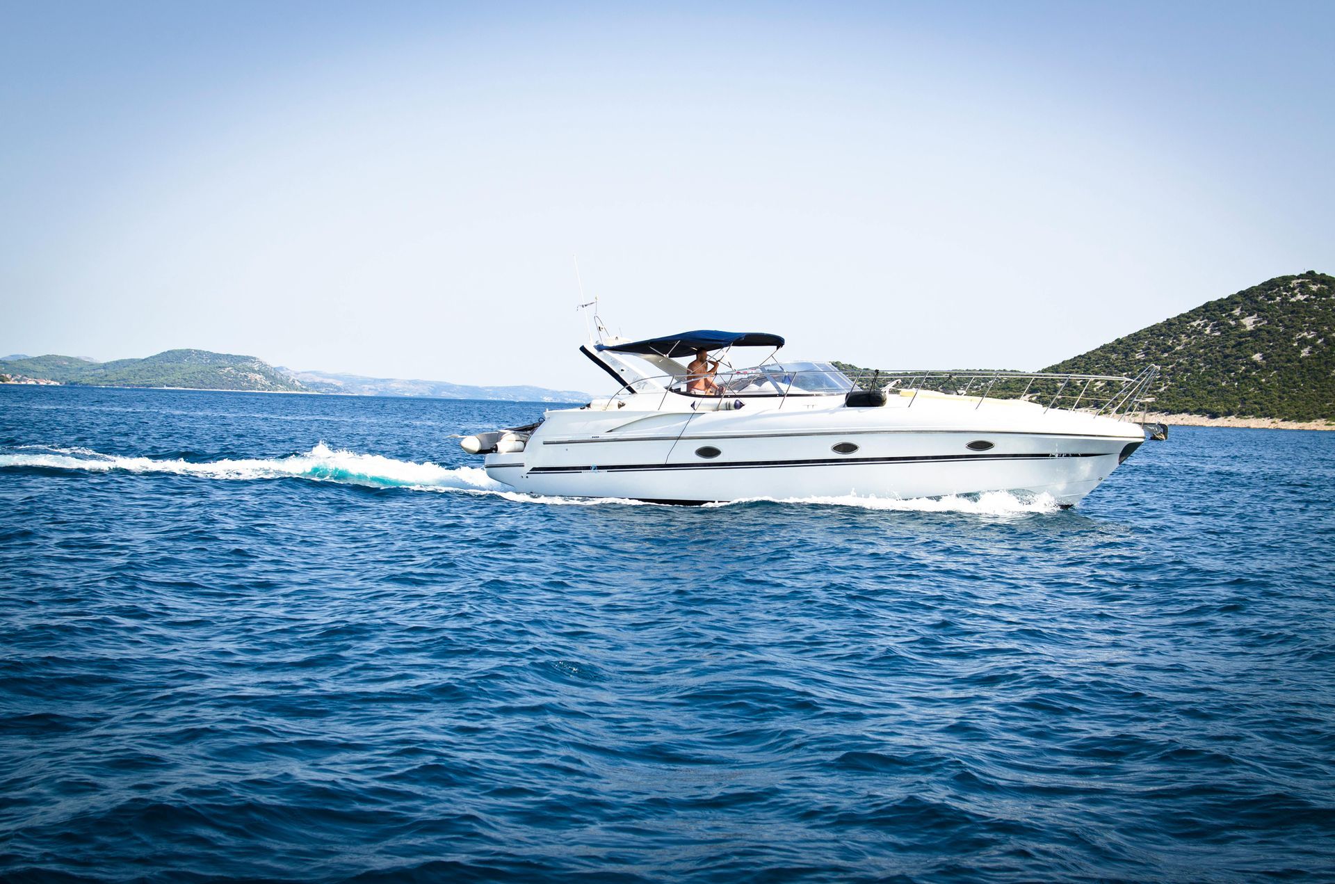 White motorboat speeding across blue water, with a forested island in the background.