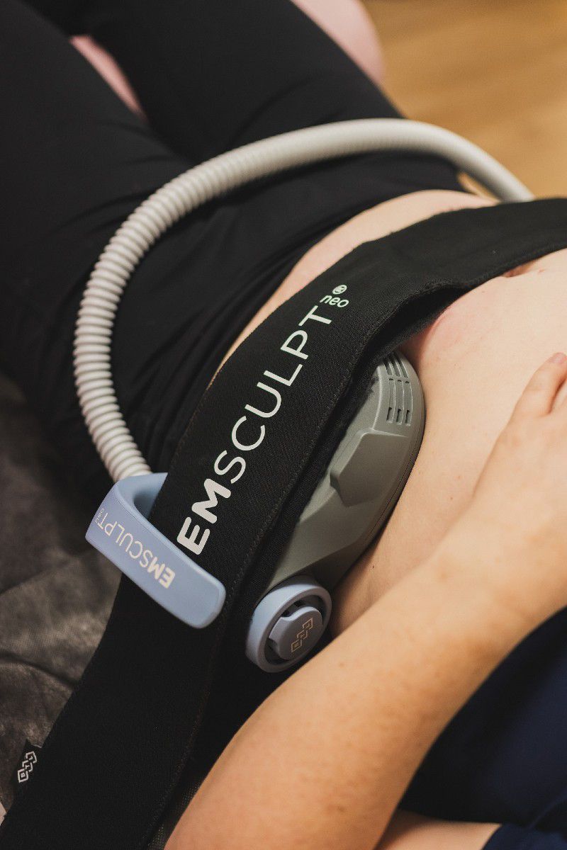 A person is laying down with a device on their stomach that says emsculpt