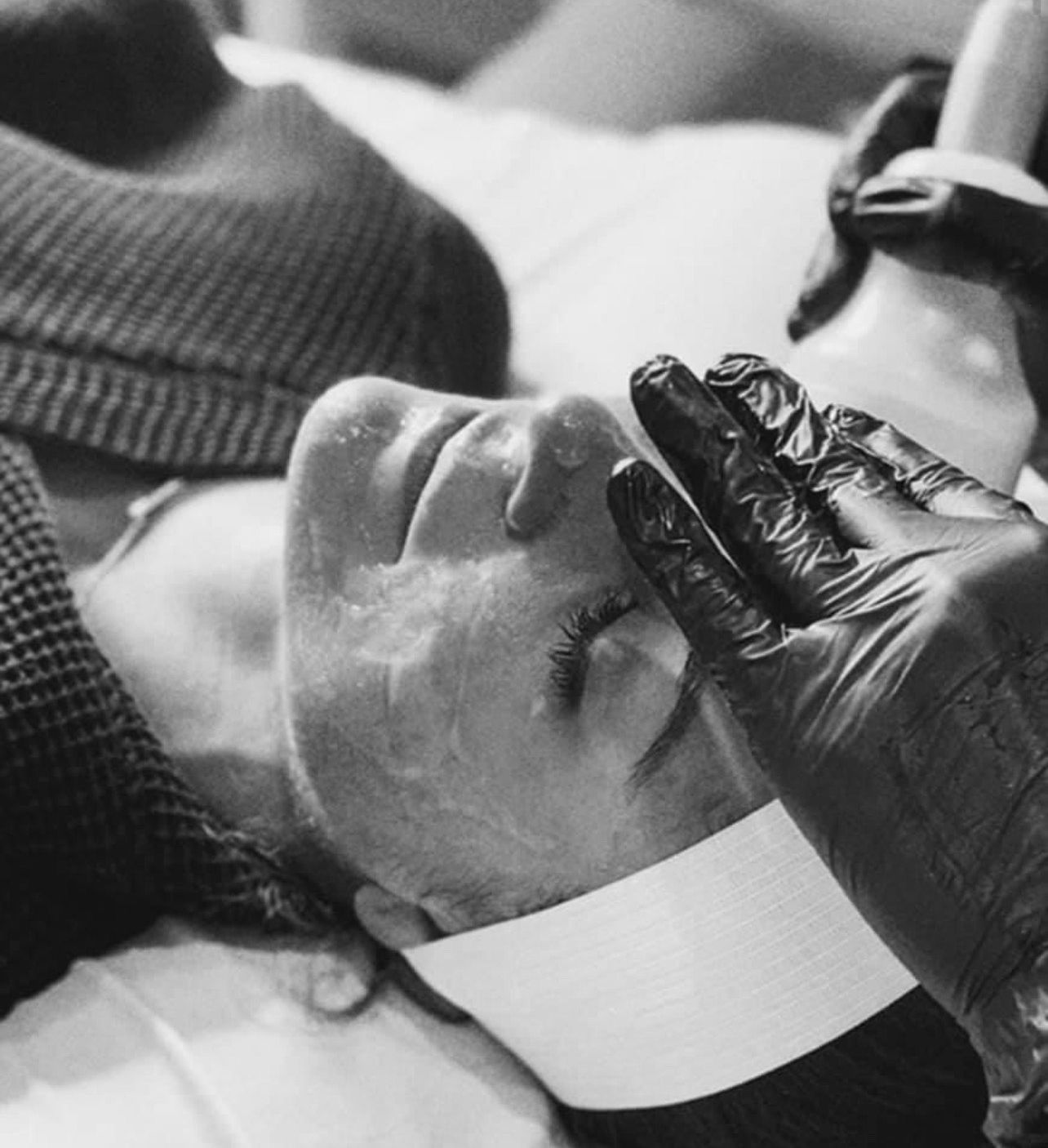 A black and white photo of a person getting a facial treatment.