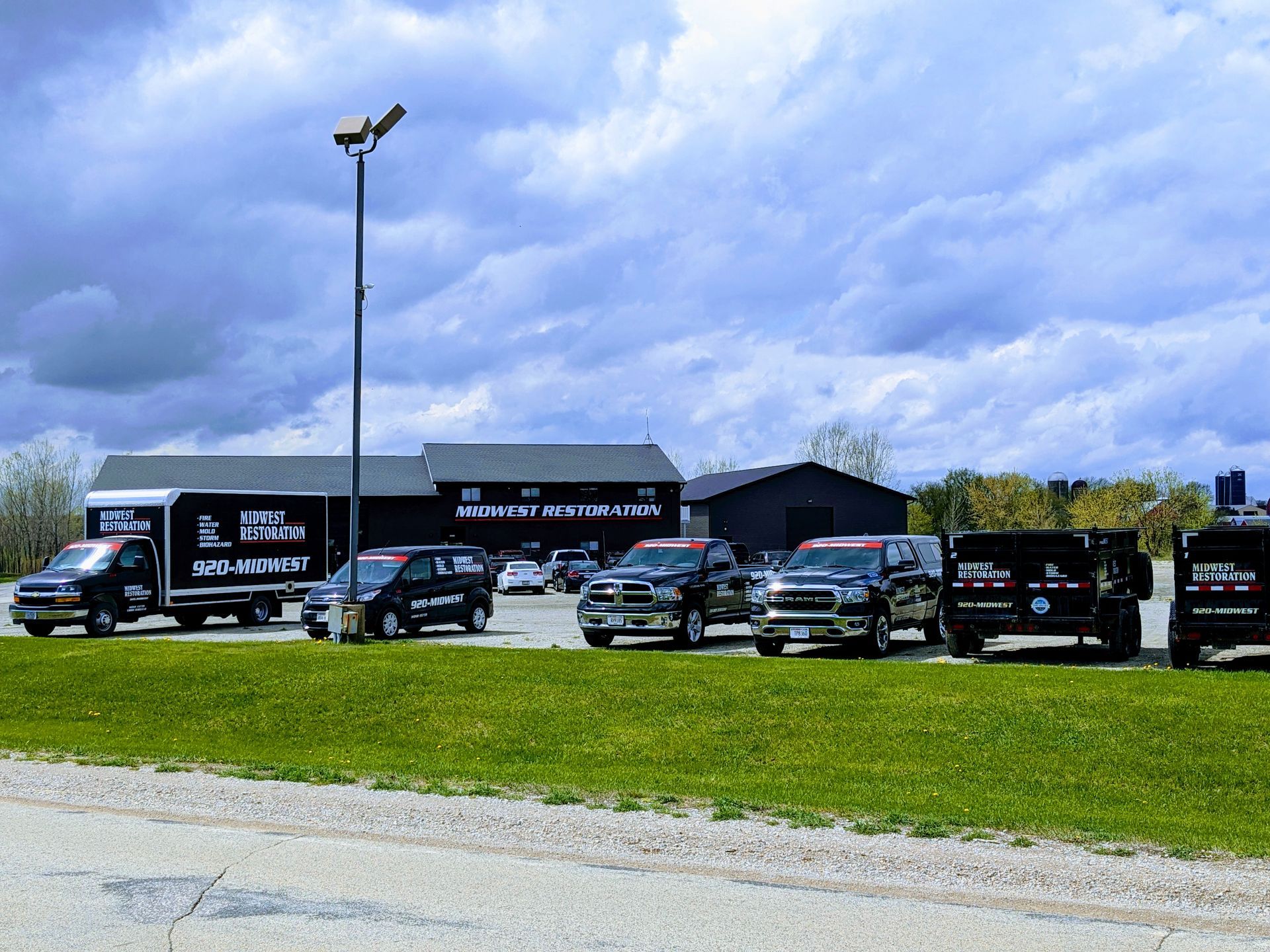 A row of trucks are parked in a parking lot in front of a building.