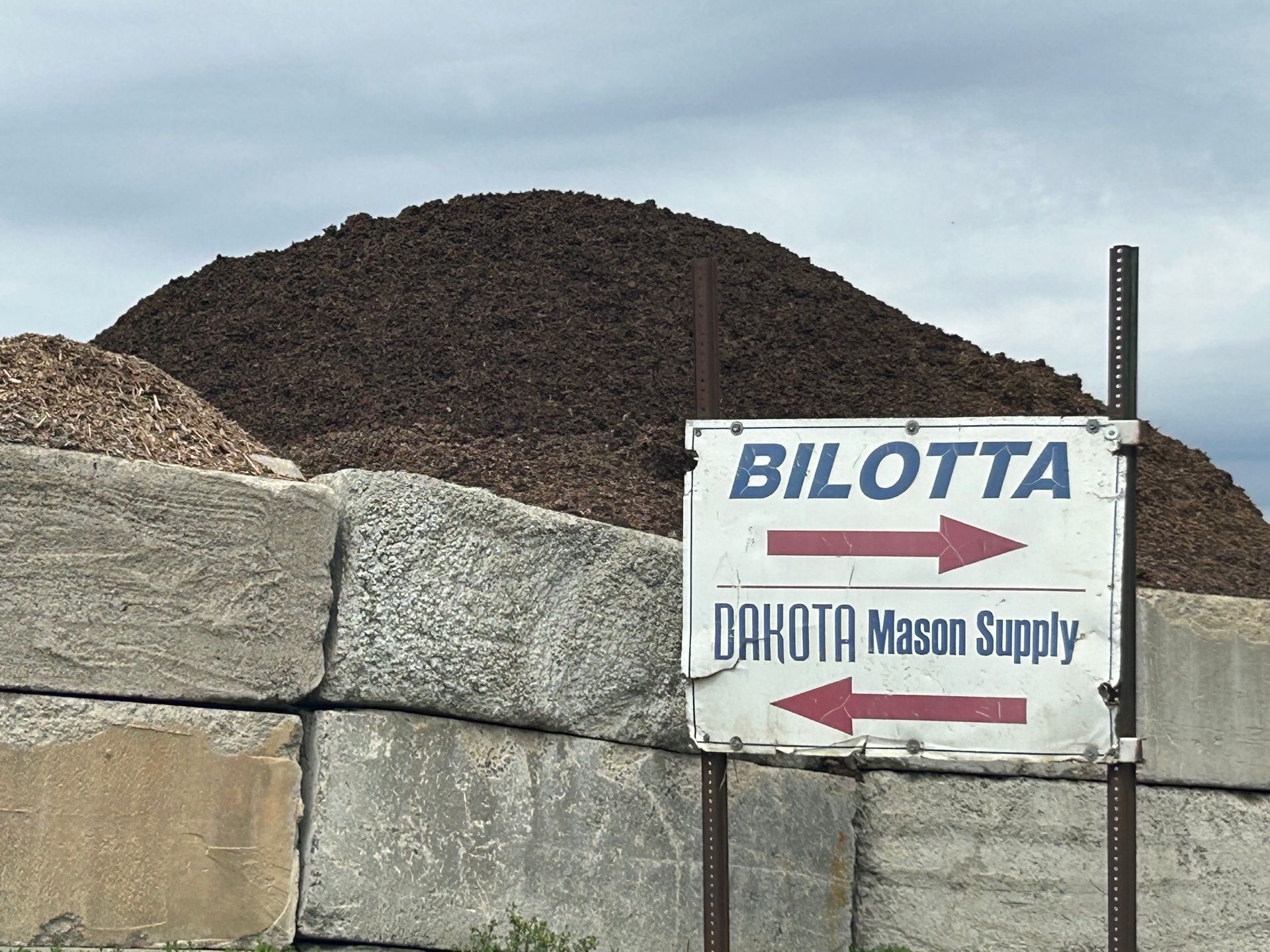A large pile of dirt is behind a sign for bilotta dakota mason supply