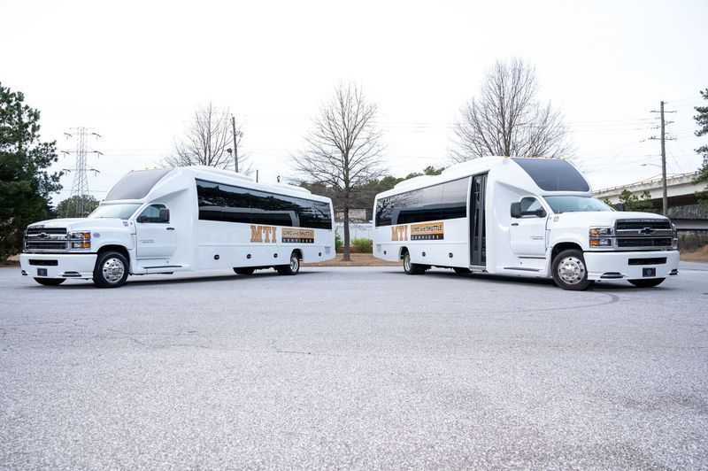 Two white shuttle buses parked side-by-side in a paved lot under a cloudy sky.