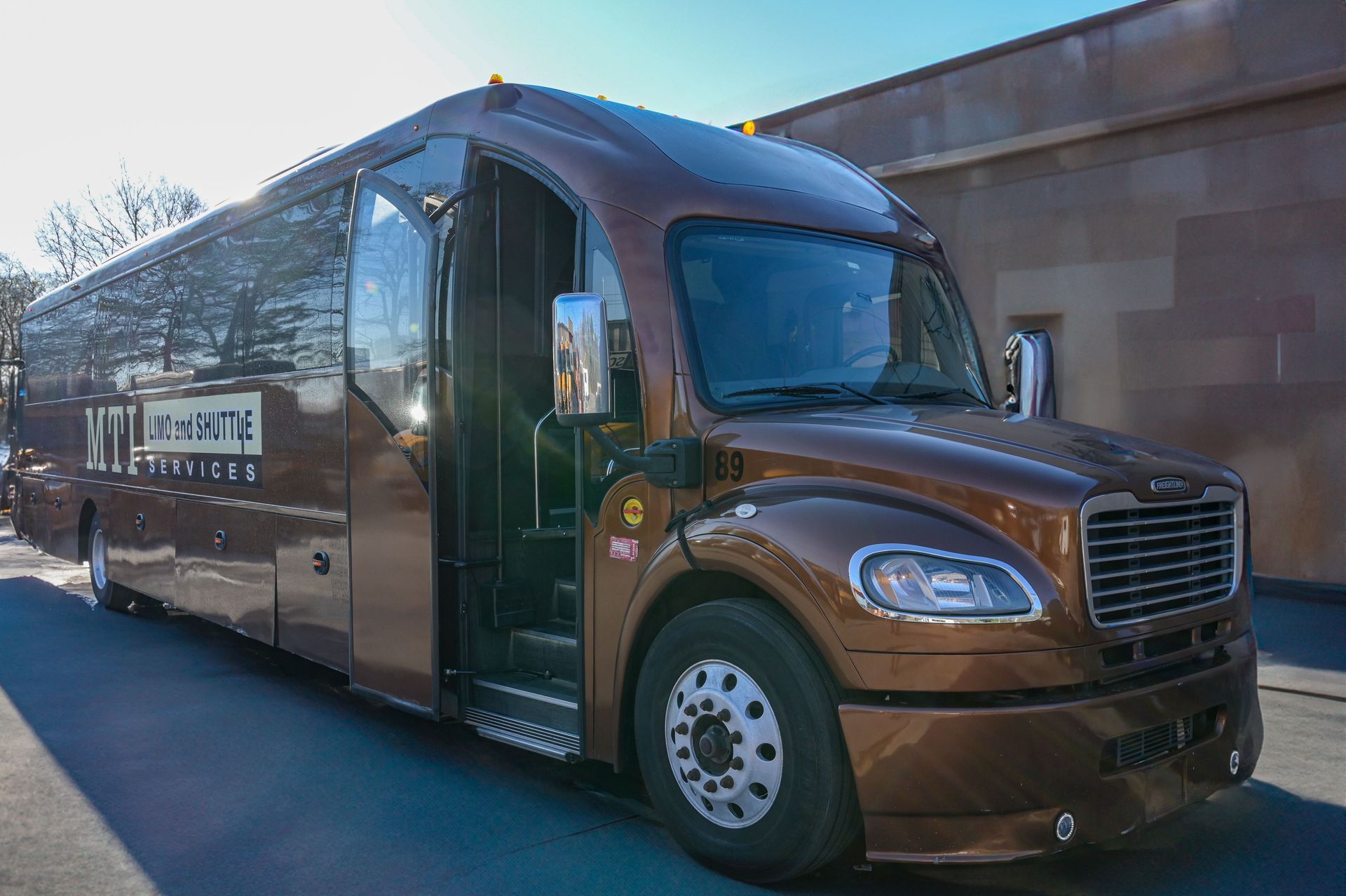 A brown shuttle bus with a partially open passenger door parked outdoors on a sunny day.