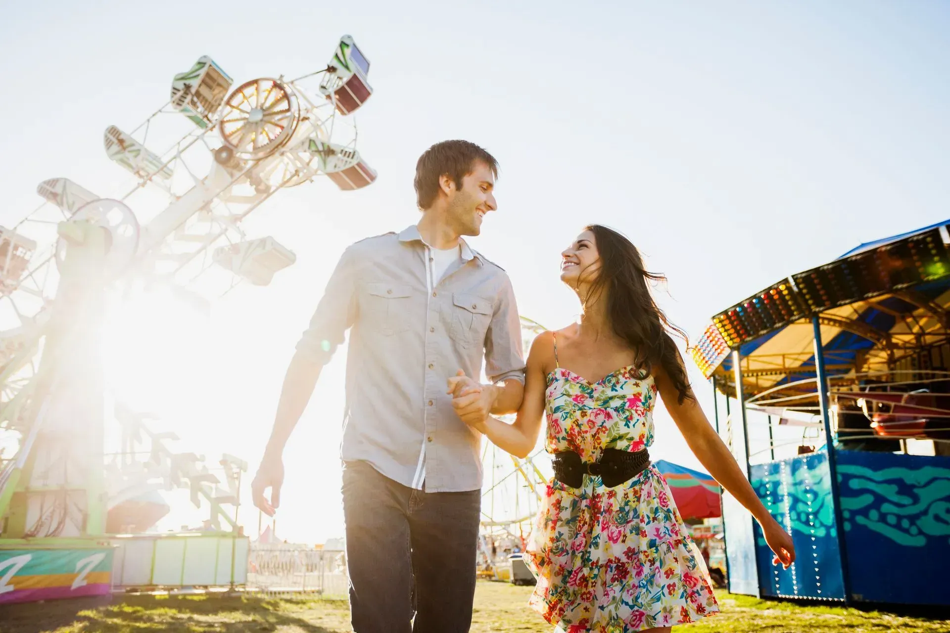 Couple walking hand in hand at a bright carnival with rides and colorful booths
