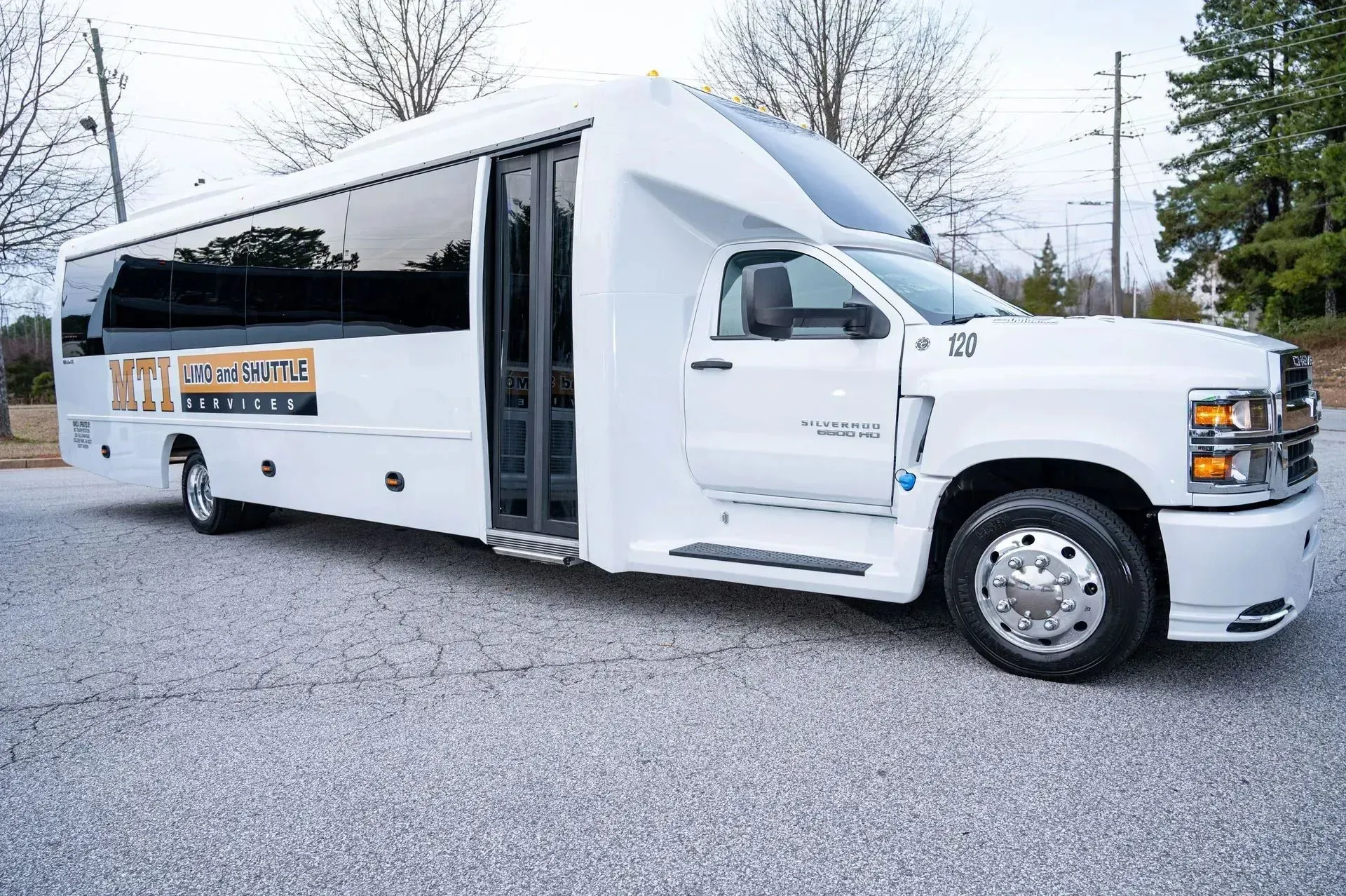 White shuttle bus parked on gravel, with extended side door and tinted windows.