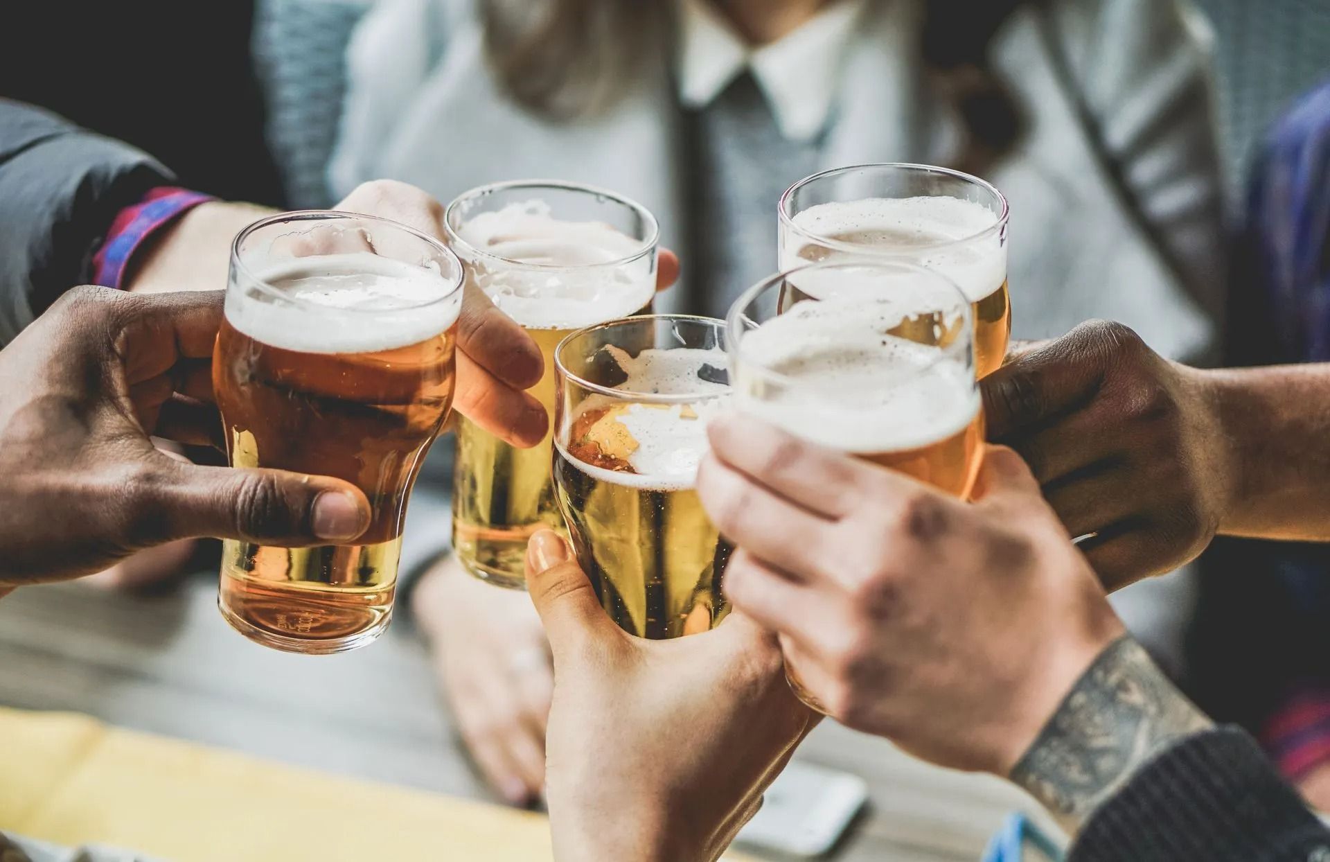 Hands clinking beer glasses in a toast at a social gathering