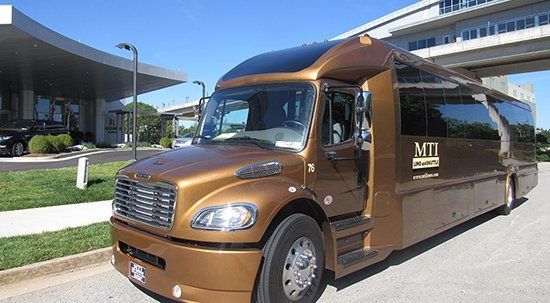 Brown shuttle bus parked outside a modern building, with a covered walkway overhead