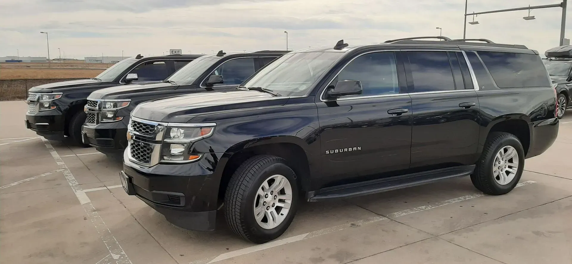 Black SUV parked in a lot beside other vehicles under an overcast sky