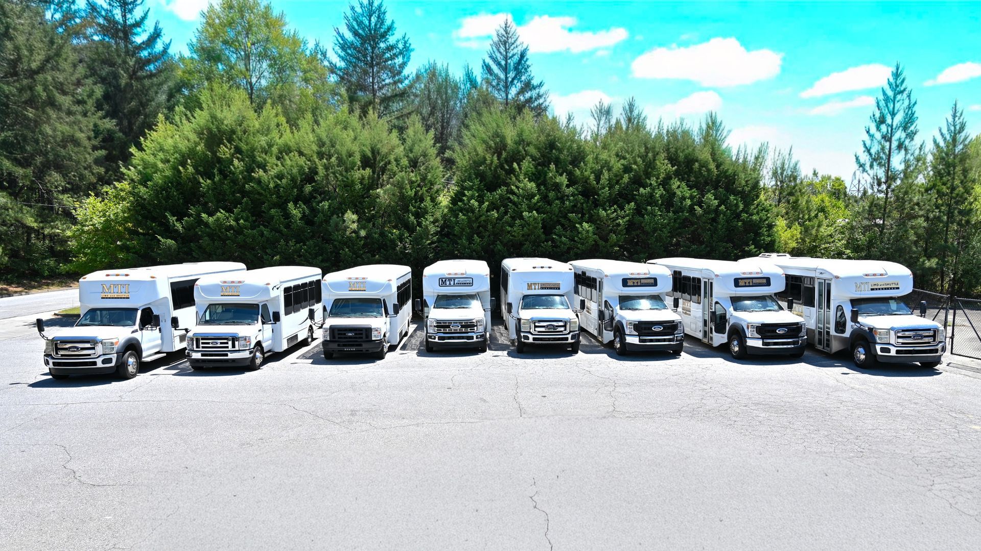 Line of white RVs and trucks parked on a lot with trees and blue sky behind them