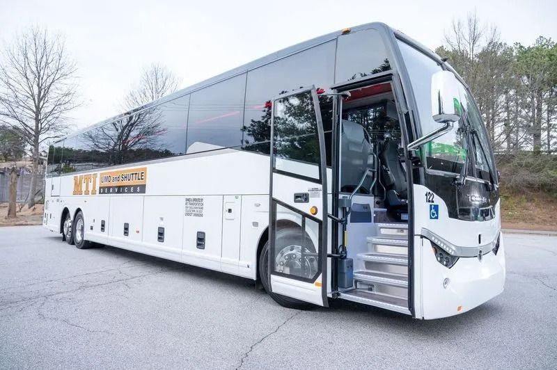 A white motorcoach bus parked on an asphalt lot with its front passenger door open, revealing steps to the interior.