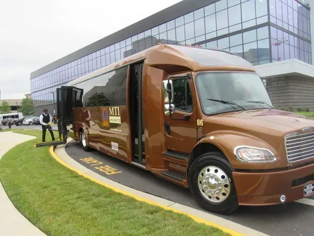 Brown tour bus parked outside a glass office building, with people nearby